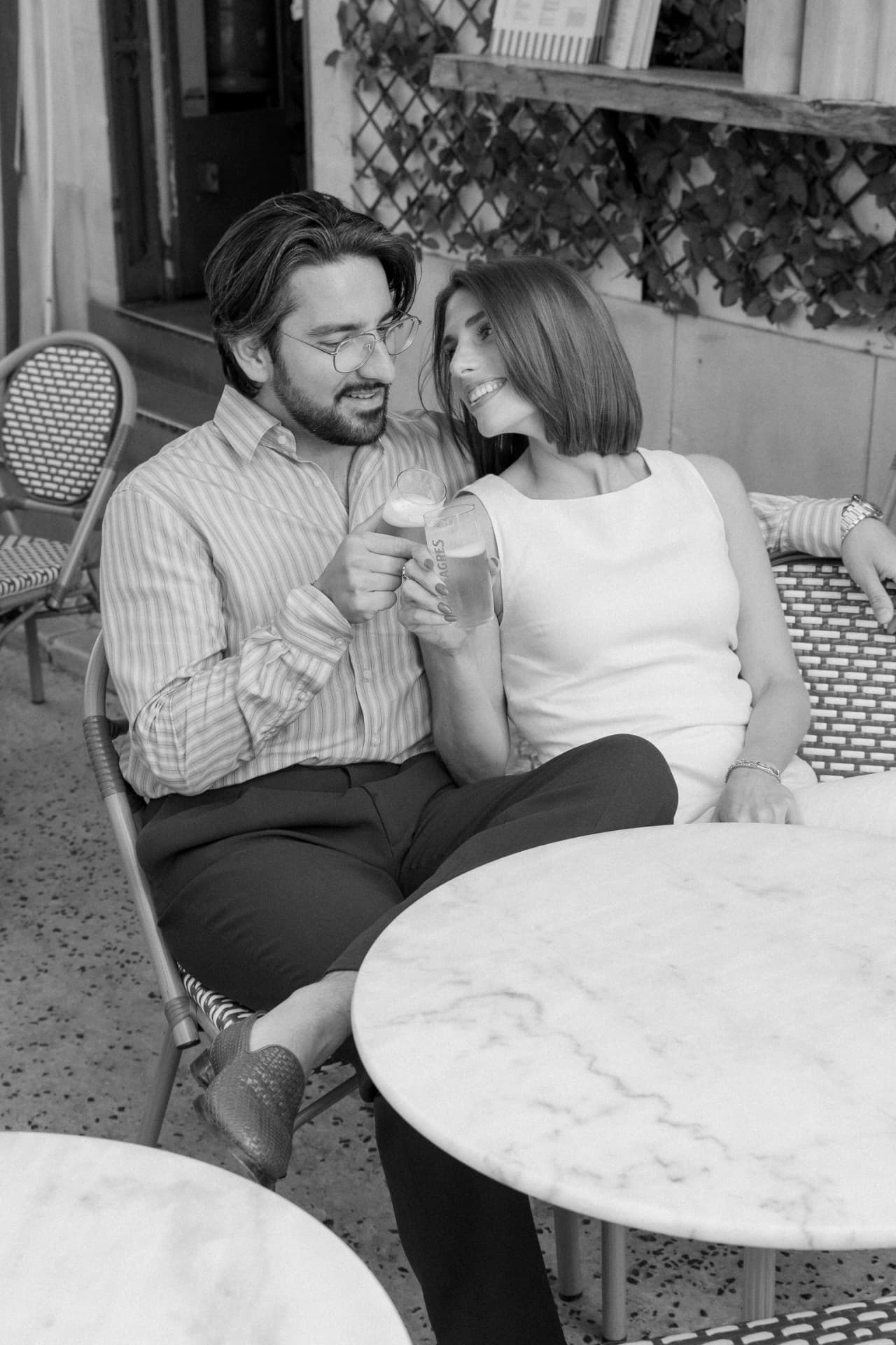 Black and white frame of the couple toasting at a pavement café