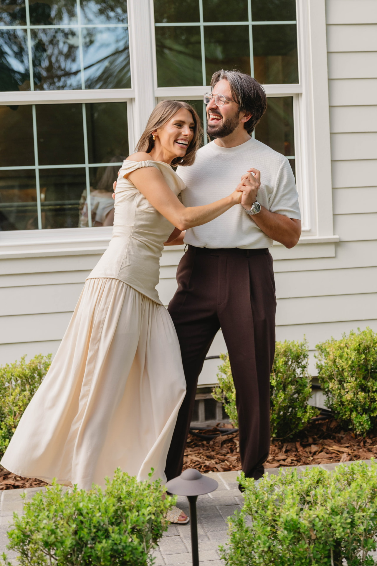 Kayla and Bruno dancing and laughing outside a white clapboard house
